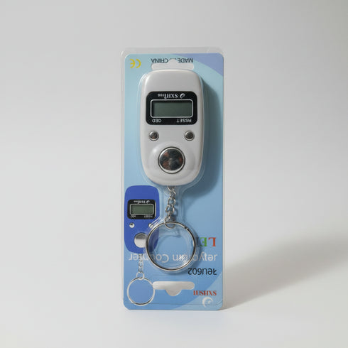 A hand holding a packaged digital pocket scale keychain. The scale is silver with a small LCD display and a blue accent, attached to a metal key ring.
