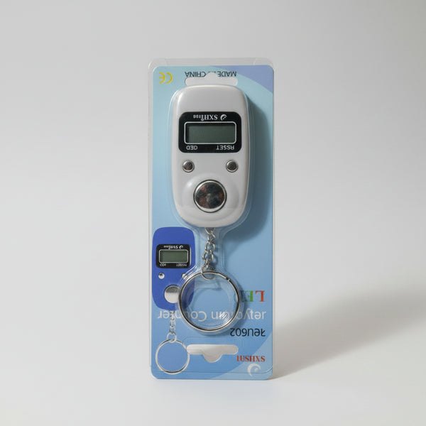 A hand holding a packaged digital pocket scale keychain. The scale is silver with a small LCD display and a blue accent, attached to a metal key ring.